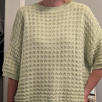 Person wearing a light green textured sweater indoors.