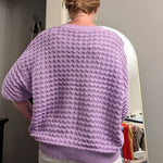 Person wearing a purple sweater standing in a room with a mirror and decor items.