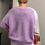 Person wearing a purple sweater standing in a room with a mirror and decor items.