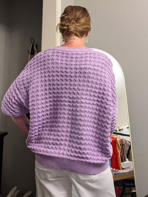Person wearing a purple sweater standing in a room with a mirror and decor items.