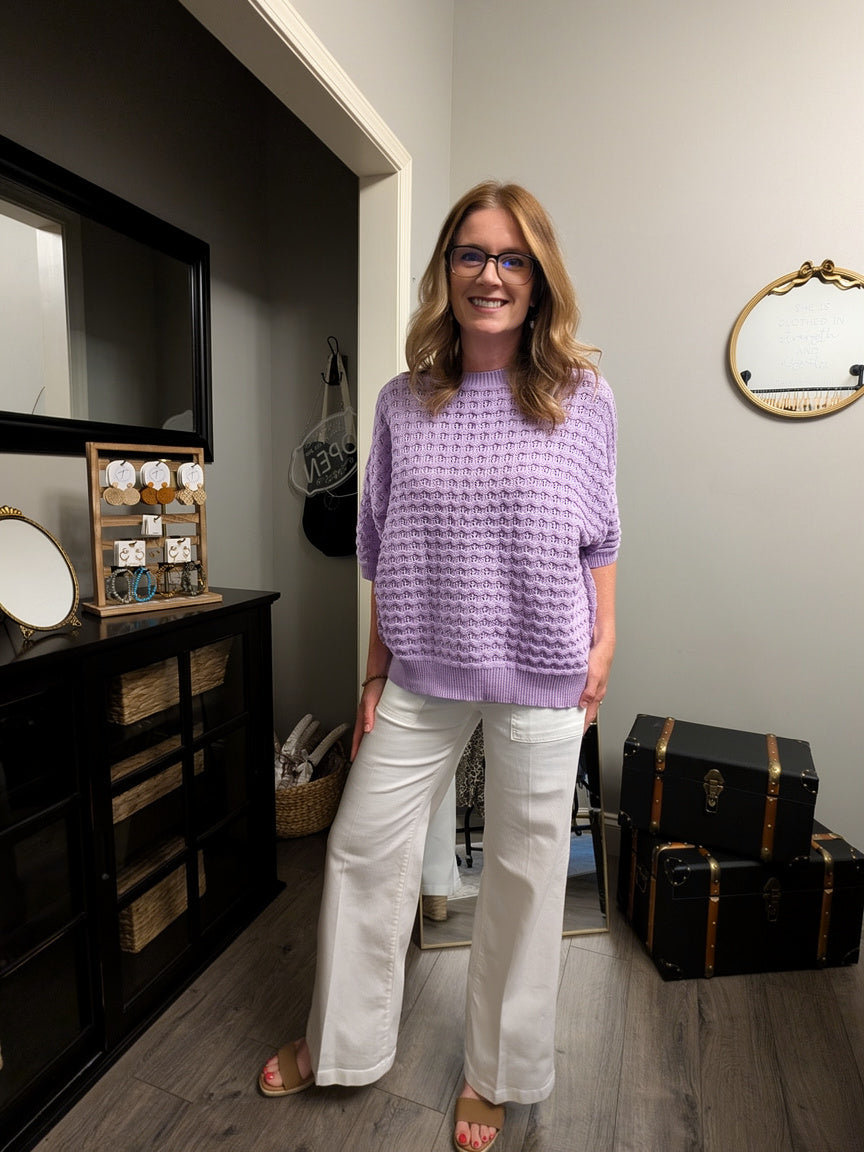 Woman in a purple sweater and white pants standing in a room with furniture and decor.