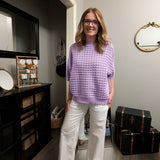 Woman in a purple sweater and white pants standing in a room with furniture and decor.